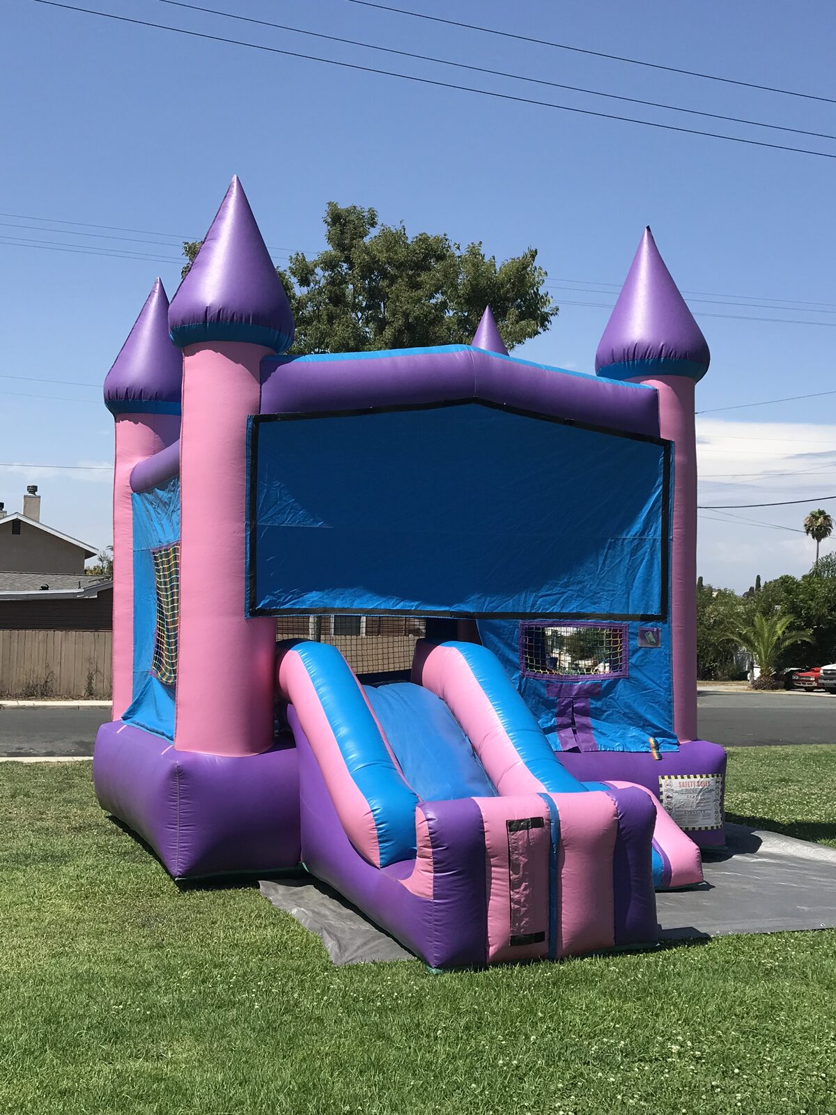 2n1 pink castle banner combo bounce house rental in San Diego, three-quarter view showing the front slide lane and castle turrets on grass