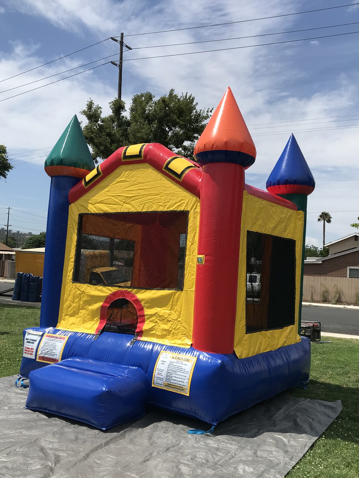 12x14 multi color castle mini bounce house rental in San Diego, angled view of all four colored turrets and safety rules placards