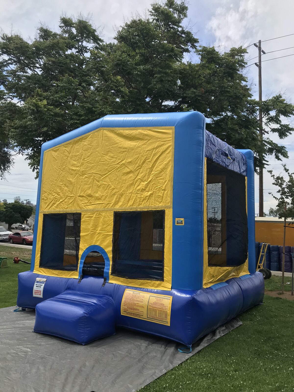 13x13 blue banner bounce house rental in San Diego — angled view over a protective tarp showing the entry ramp and mesh safety windows