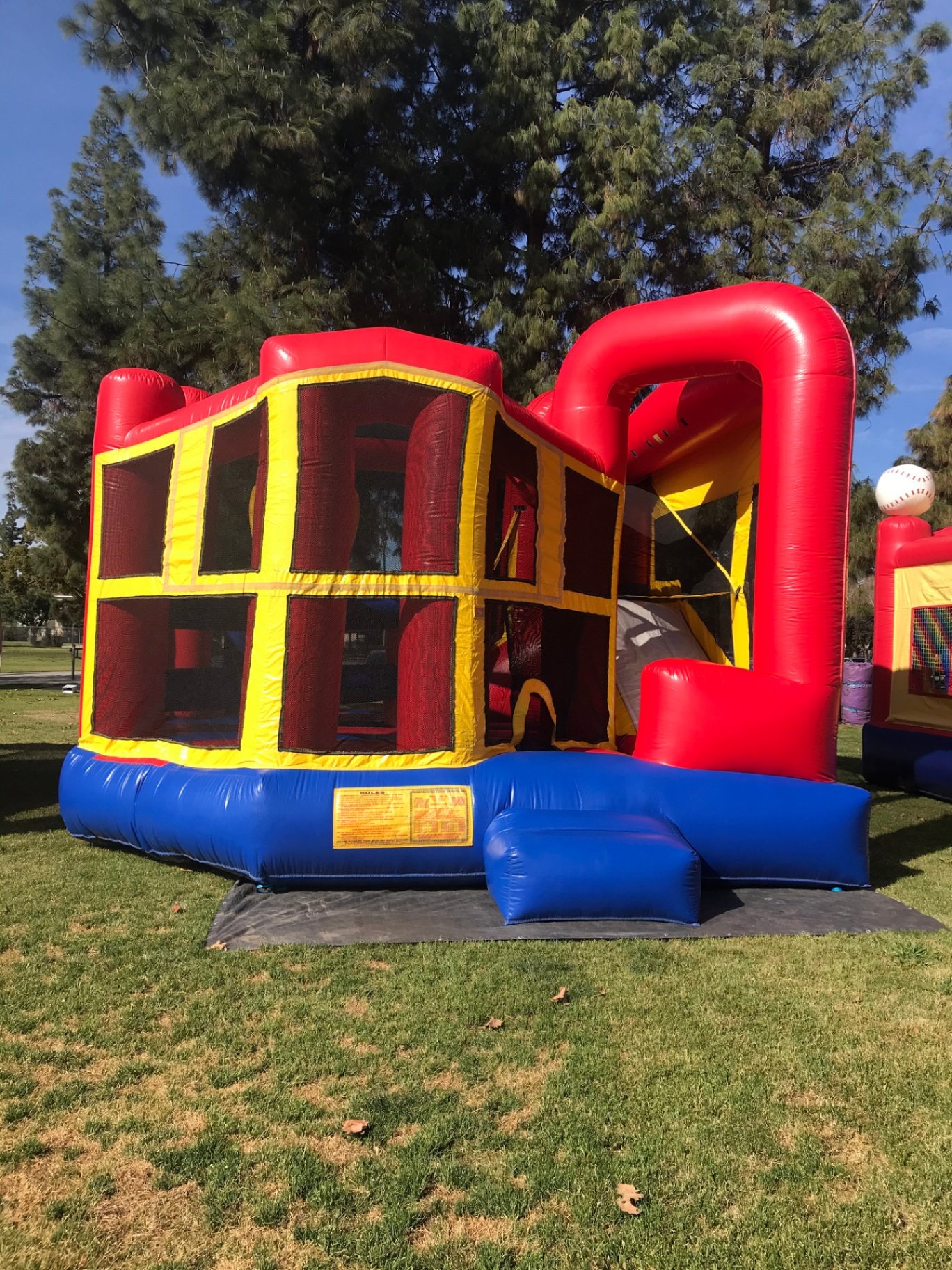 5n1 blue banner combo bounce house rental in San Diego, front view of the red, yellow and blue combo with mesh jump windows and side slide set up on a tarp on grass