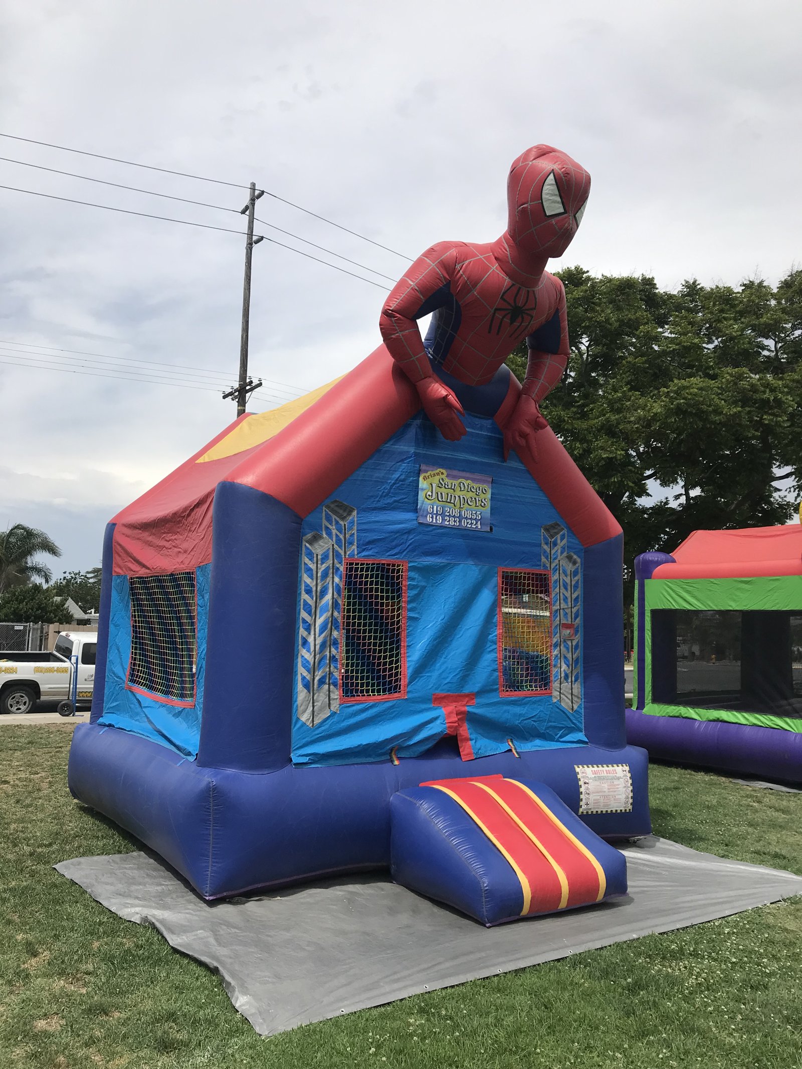 13x13 Spider-Man bounce house rental in San Diego — angled front view on a protective tarp showing the entry ramp and mesh safety windows