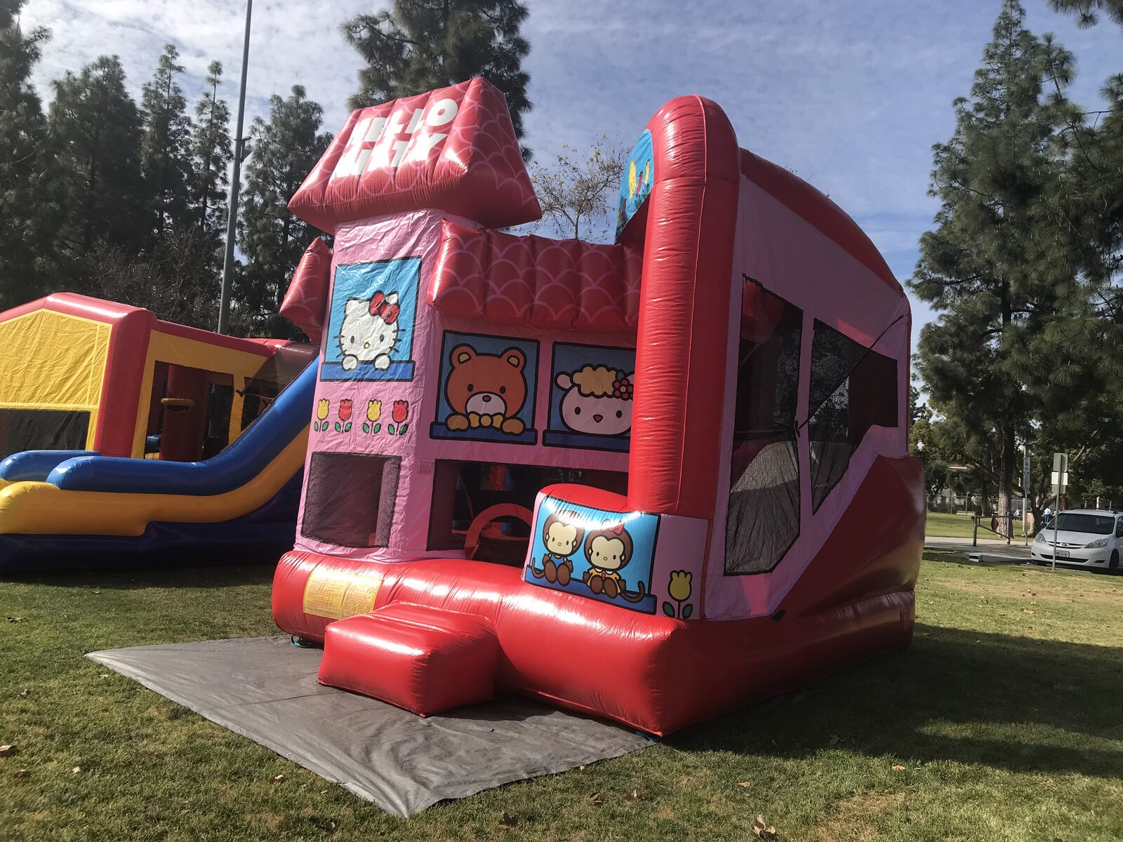 5n1 hello kitty combo bounce house rental in San Diego, three-quarter view showing the mesh side windows and slide tower on park grass