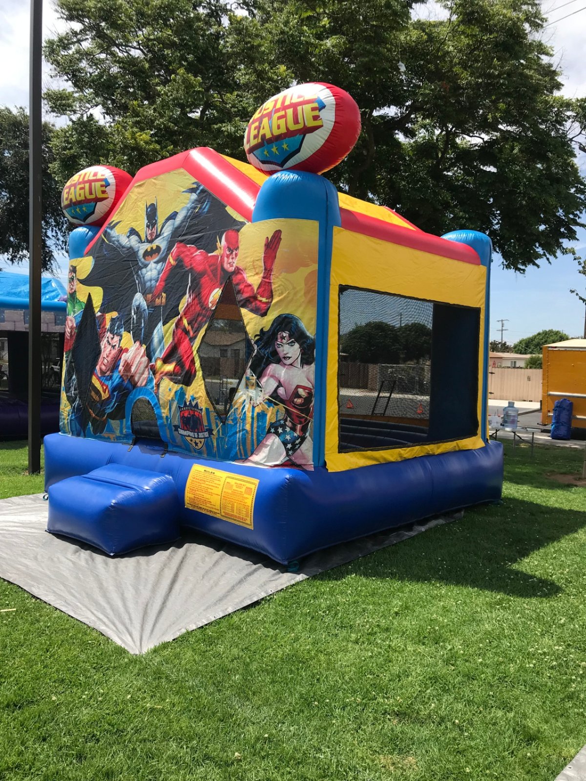 13x13 Justice League bounce house rental in San Diego — three-quarter view with yellow and blue side walls and safety ramp