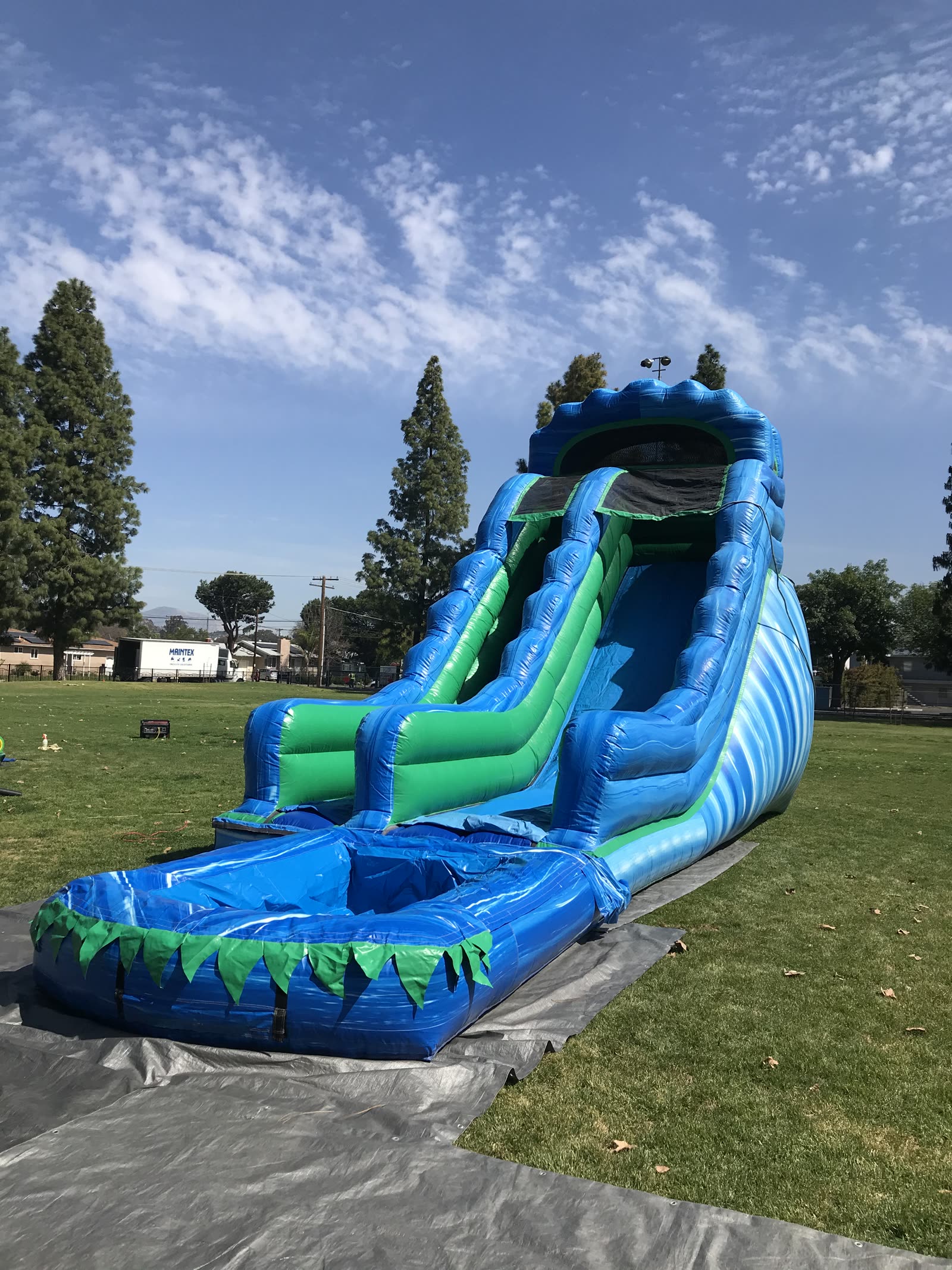 Water slide rental in San Diego, 20ft green and blue water slide angled view on grass showing the full slide lane