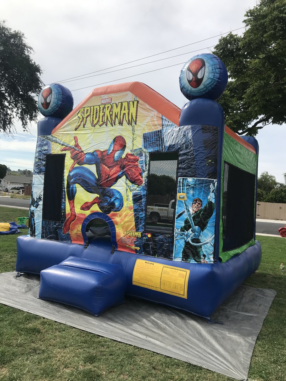 13x13 Original Spider-Man bounce house rental in San Diego — angled front view on a protective tarp showing the entry ramp and rules panel
