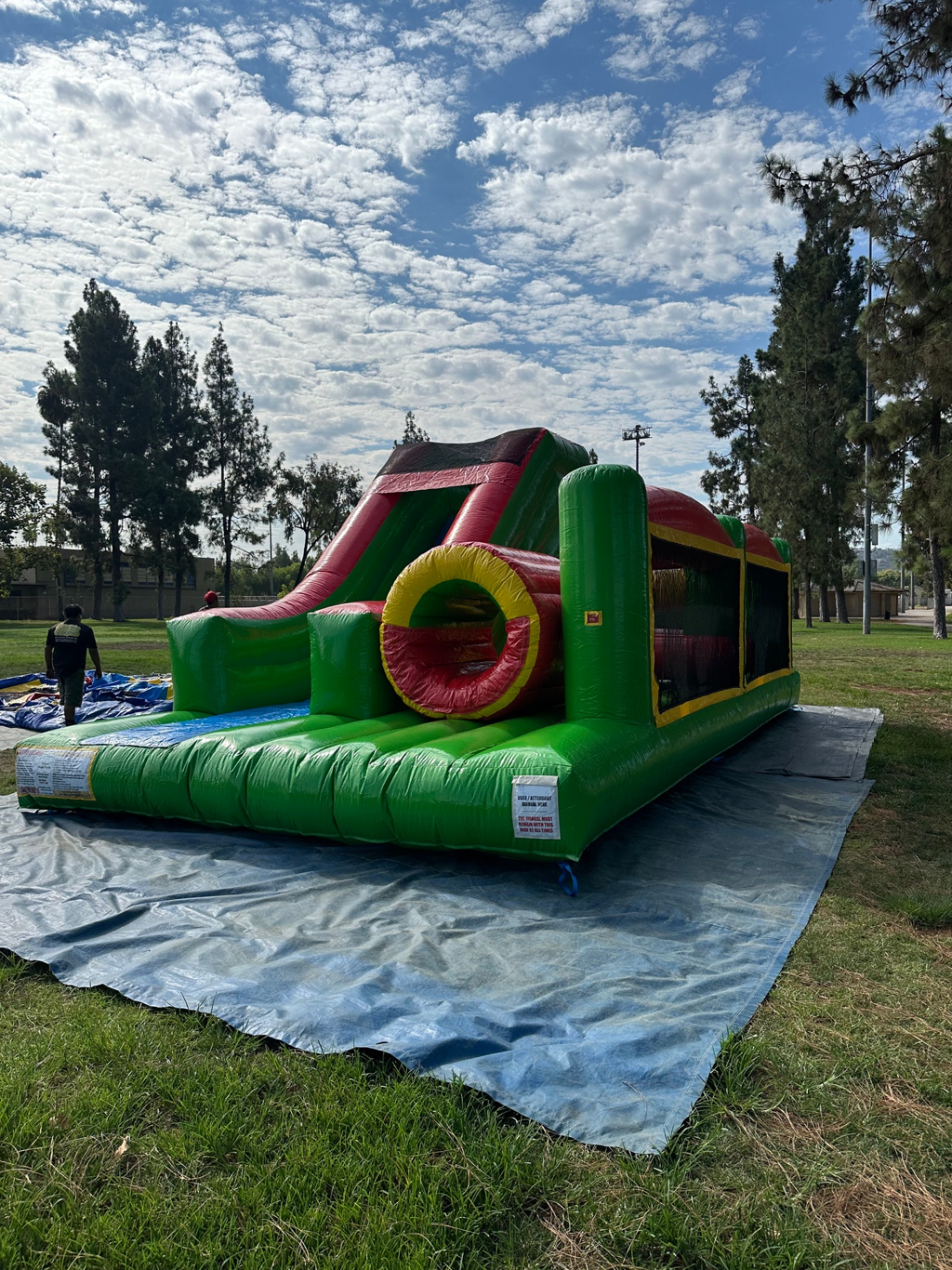 Challenge course obstacle rental in San Diego, green and red lane, three-quarter view of the slide end and crawl tunnel on a park lawn