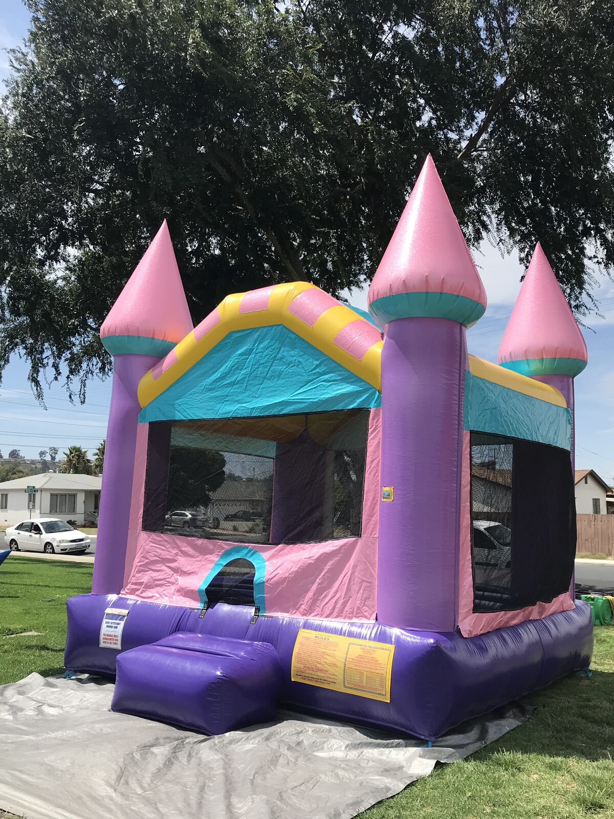 13x13 Dazzling Castle bounce house rental in San Diego — angled view on a shaded grass lawn over a protective tarp