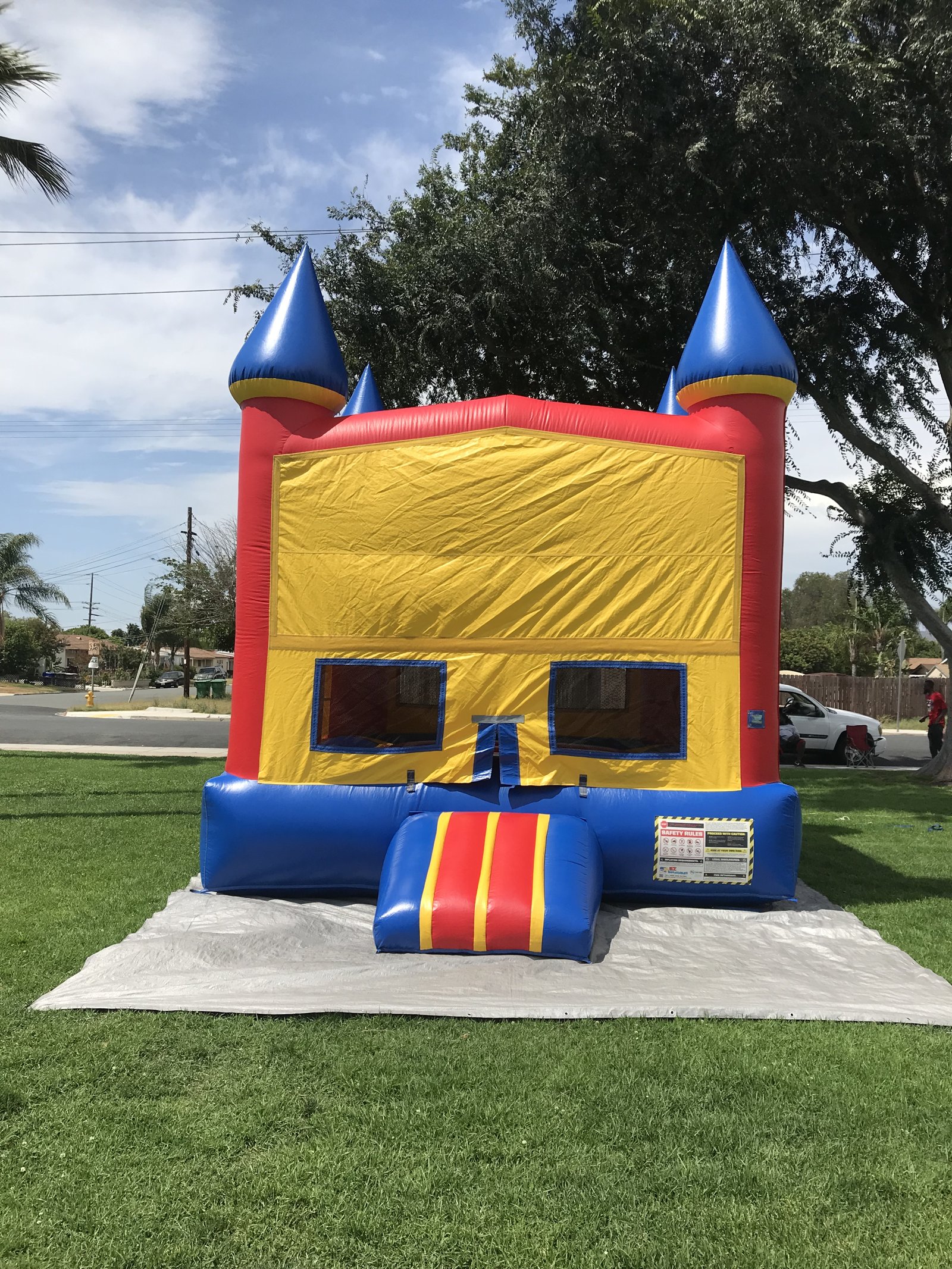 13x13 Blue Castle Banner bounce house rental in San Diego — straight-on front view of the red, yellow, and blue castle with blank banner panel and blue turret toppers on a grass lawn