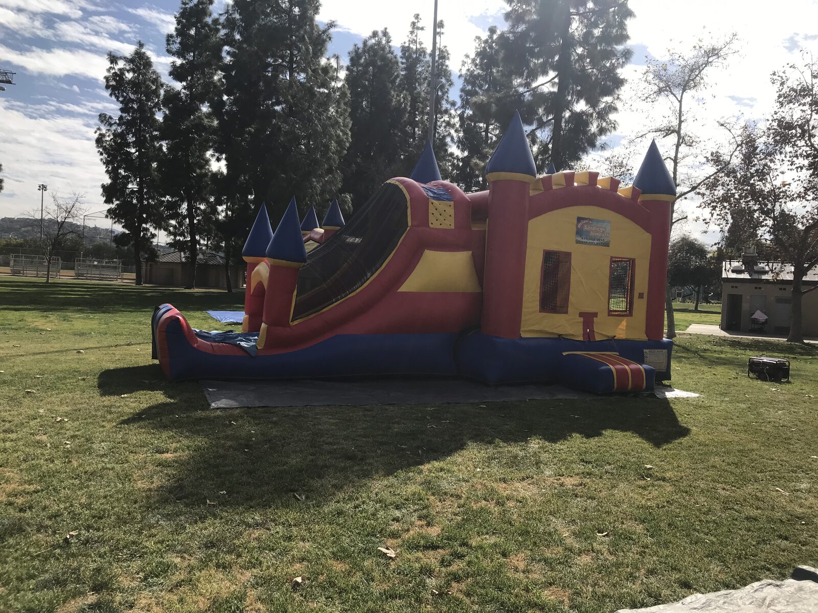 4n1 blue castle combo bounce house rental in San Diego, wider side view showing the full slide lane and entry step on a tarp