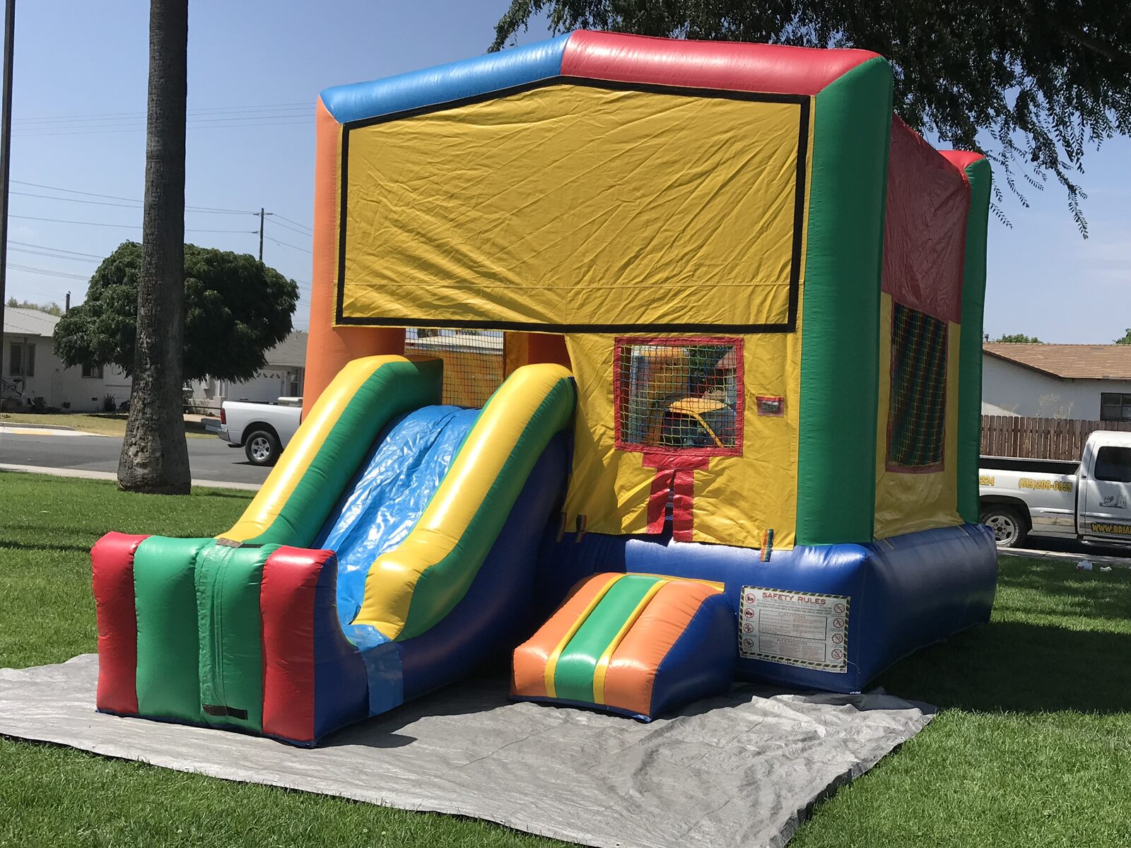 2n1 multi color castle banner combo bounce house rental in San Diego, three-quarter view of the slide and orange entry step on a tarp over grass