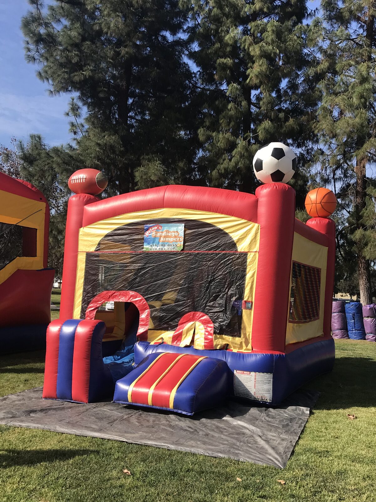5n1 sports combo bounce house rental in San Diego, three-quarter view of the unit set up on park grass with the entry ramp and safety rules placard
