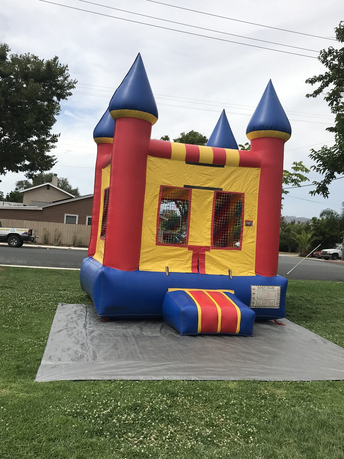 12x14 blue castle mini bounce house rental in San Diego, angled front view on a tarp in a grassy yard