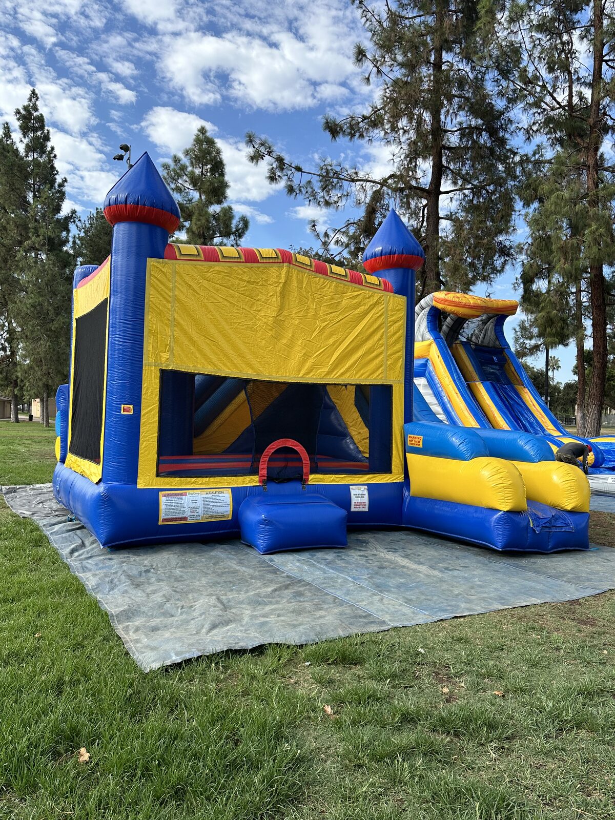 6n1 blue castle banner combo bounce house rental in San Diego, wide park view of the full unit staked on a tarp on grass under blue skies