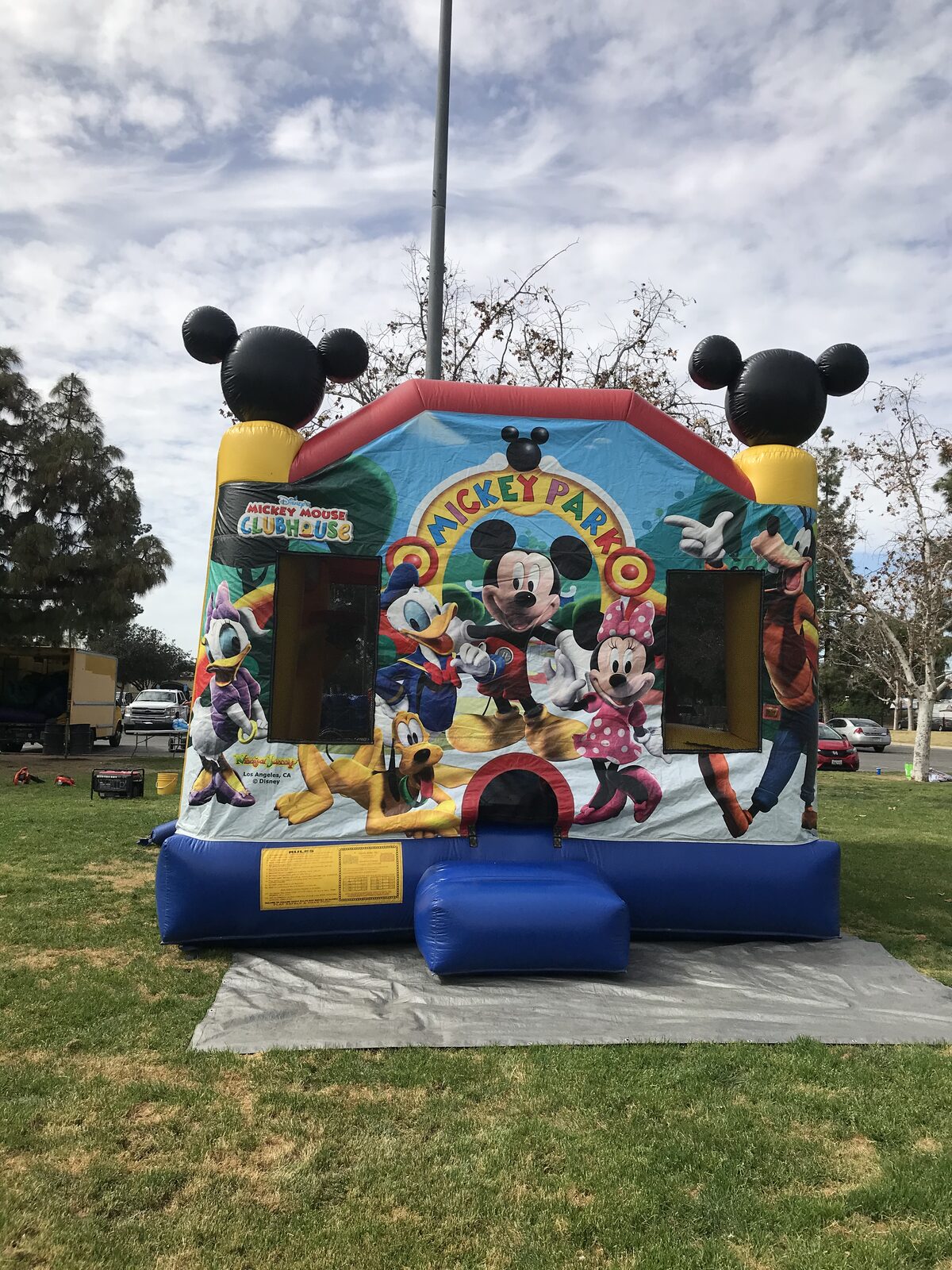 4n1 Mickey combo bounce house rental in San Diego, front view of the Mickey Mouse Clubhouse art panel with 3D Mickey ears on the towers, set up on a tarp at a park