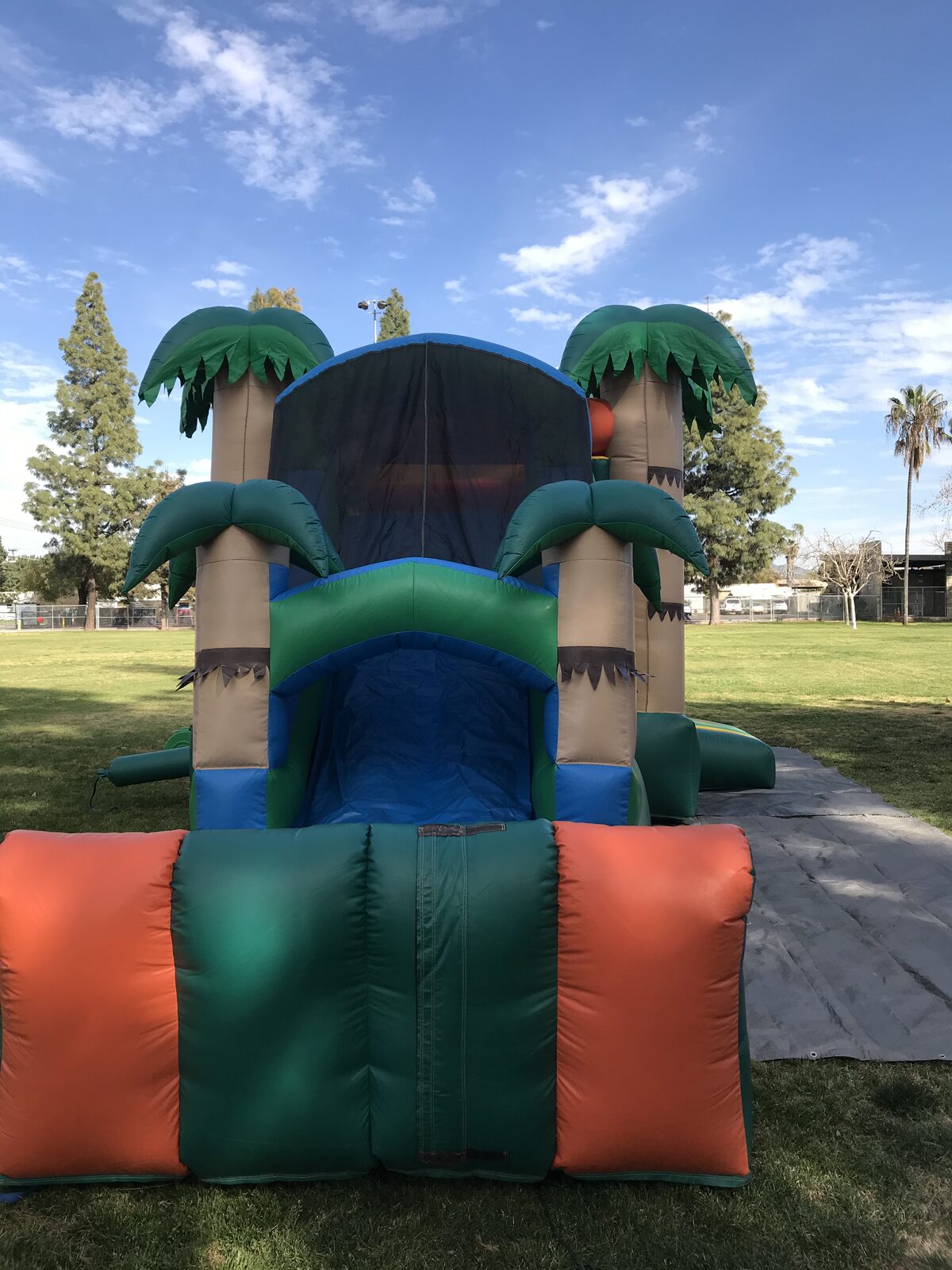4n1 palm tree combo bounce house rental in San Diego, single slide version, wide view of the full unit staked down on a tarp