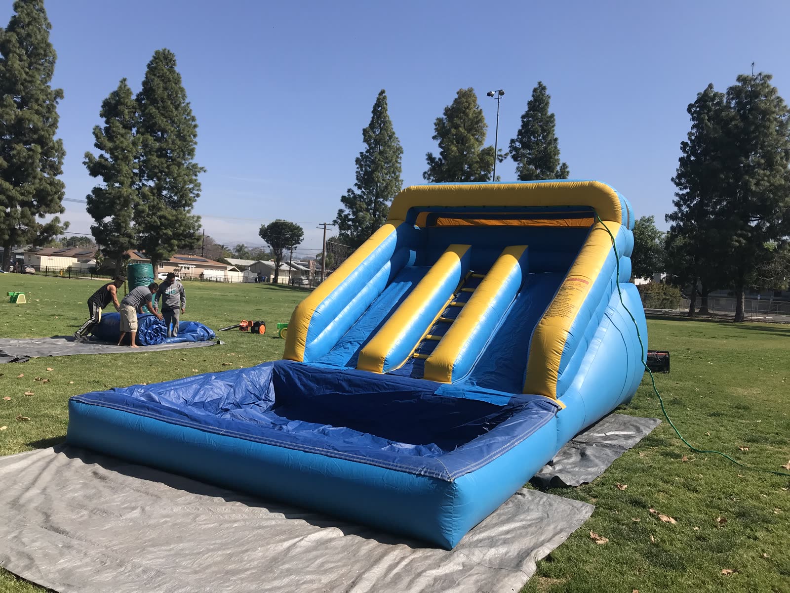 Mini water slide rental in San Diego, 12ft mini dual lane slide set up on a park lawn with the crew finishing setup nearby