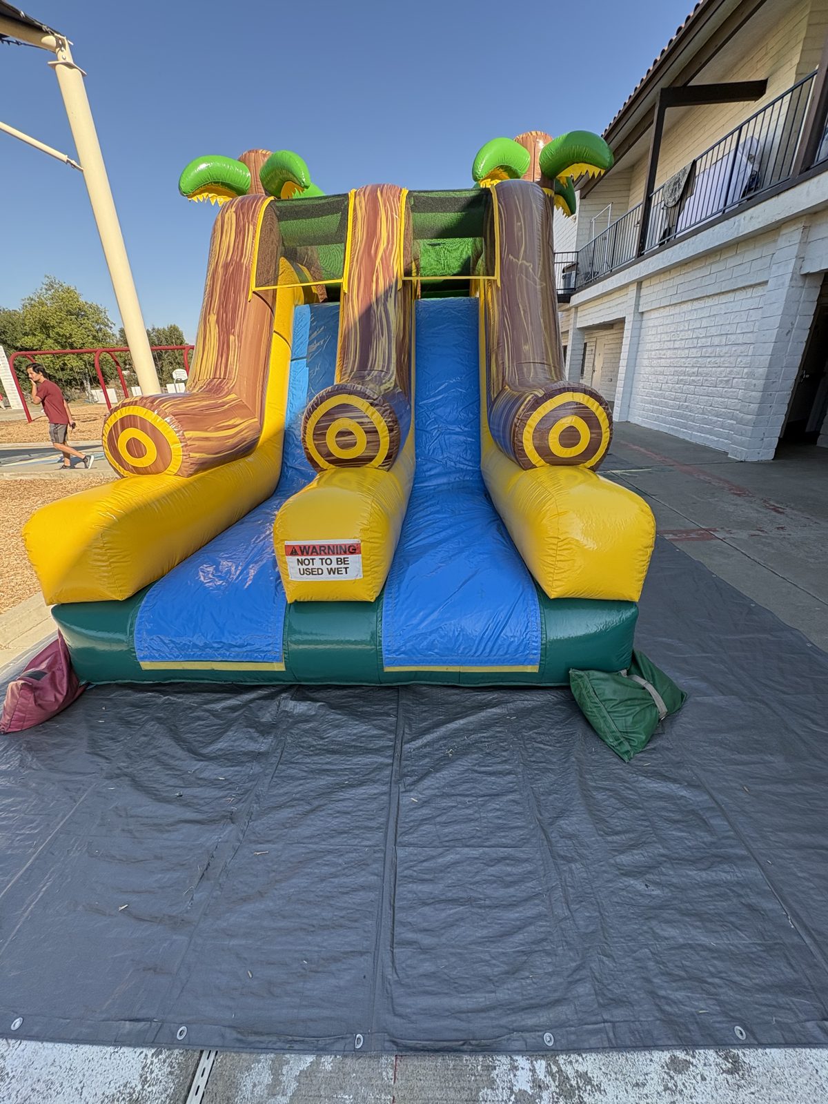 4n1 tropical oasis dual slide combo bounce house rental in San Diego, front view of the blue and yellow dual slide lanes with palm tree pillars