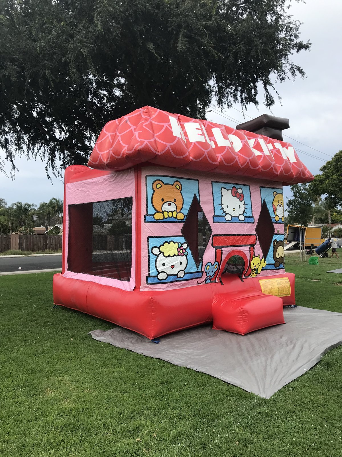 13x13 Hello Kitty bounce house rental in San Diego — angled view on a park lawn over a protective tarp with the entry ramp in front