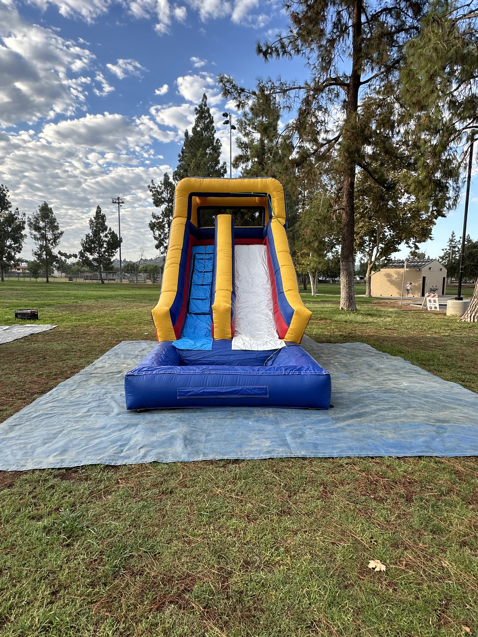 Water slide rental in San Diego, 15ft multi color setup front view on a park lawn showing the climbing lane and splash pool on a tarp