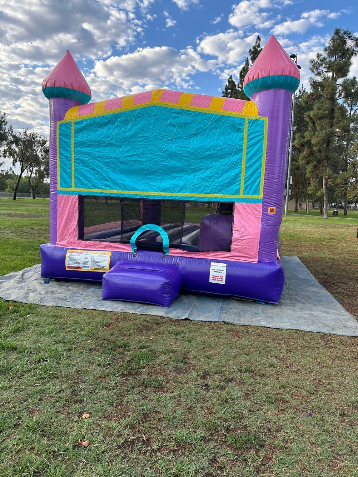 4n1 dazzling castle combo bounce house rental in San Diego, straight-on front view of the pink, purple, and teal castle with blank banner panel and purple entry step