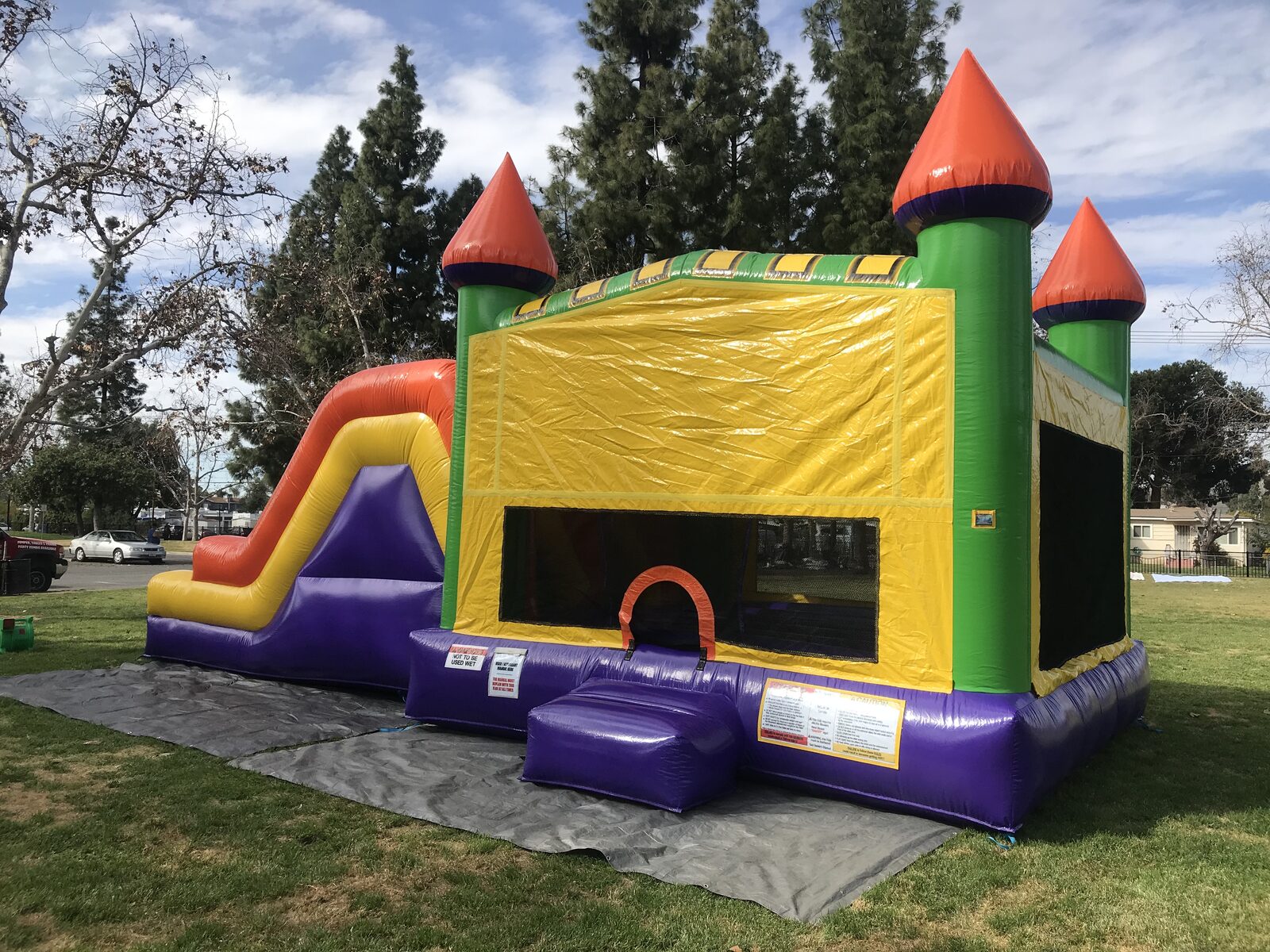 4n1 multi-color castle banner combo bounce house rental in San Diego, rear three-quarter view of the yellow banner panel, arched entry and slide staked on a tarp