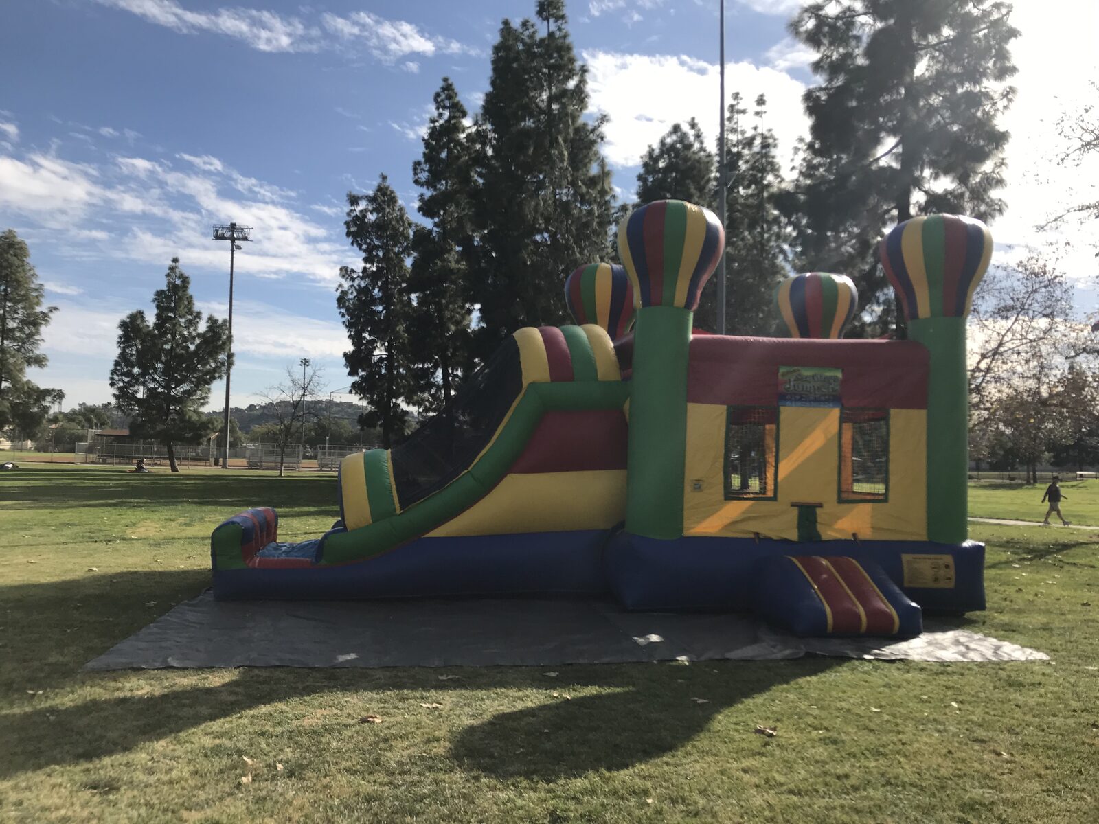4n1 balloon castle combo bounce house rental in San Diego, side view of the green, red, and yellow unit with hot-air-balloon towers and attached slide on park grass