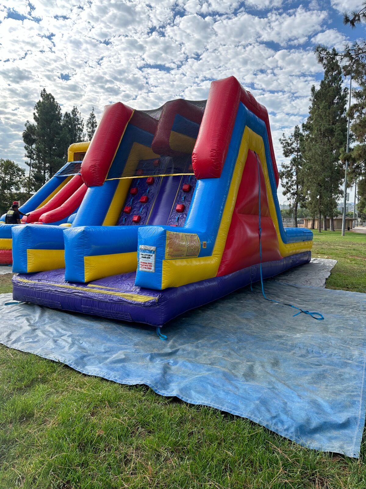 18ft dual lane monster obstacle course rental in San Diego, angled view of the slide side set up on a tarp at a park