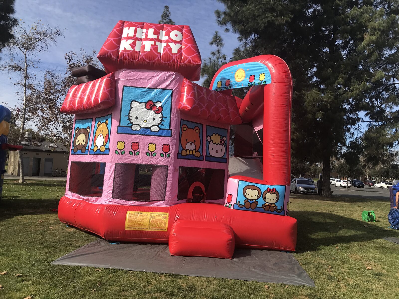 5n1 hello kitty combo bounce house rental in San Diego, pink and red Hello Kitty house-style combo with the covered side slide set up on a tarp at a park
