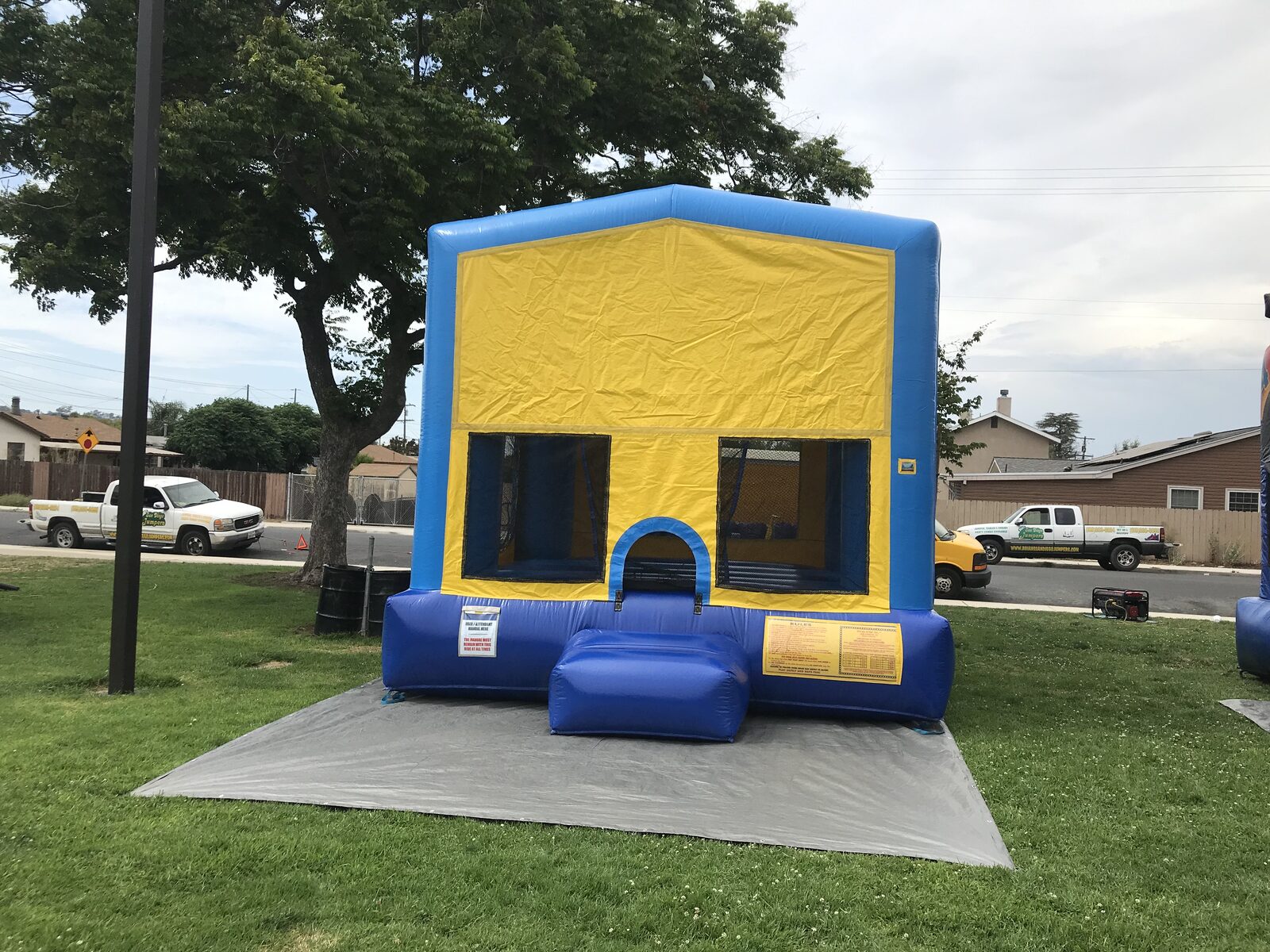 13x13 blue banner bounce house rental in San Diego — straight-on front view with blue frame, blank yellow banner panel, and blue base on a park lawn