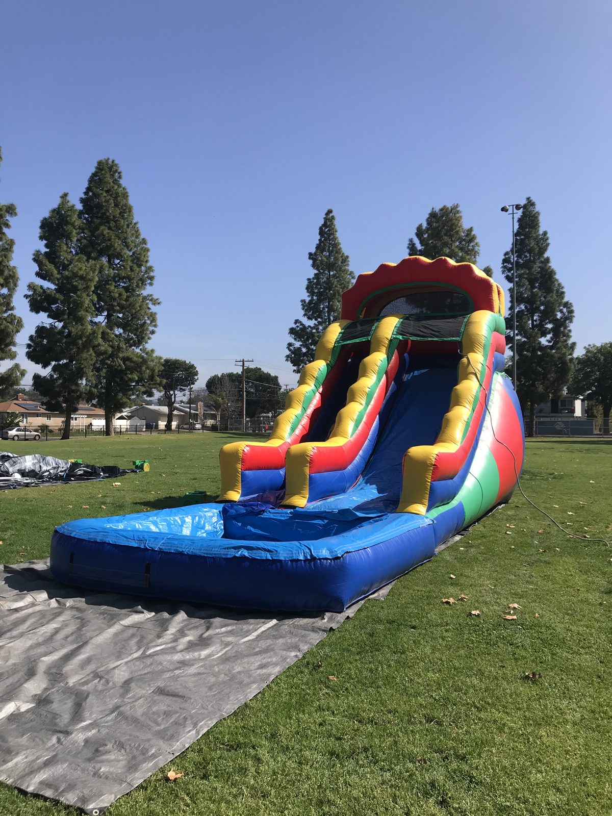 Water slide rental in San Diego, 18ft multi color setup angled view on a park lawn showing the full slide lane
