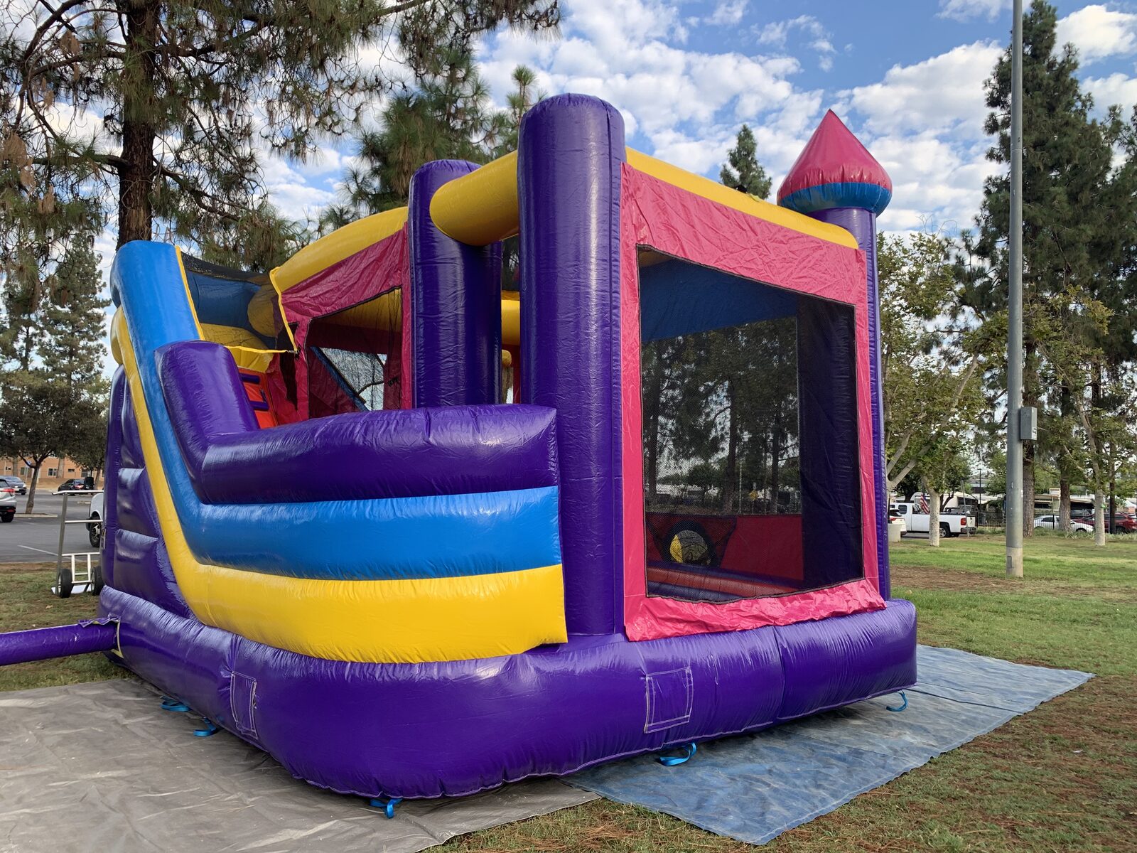 6n1 dream castle combo bounce house rental in San Diego, purple, pink and yellow castle with blue side slide set up on a tarp at a park