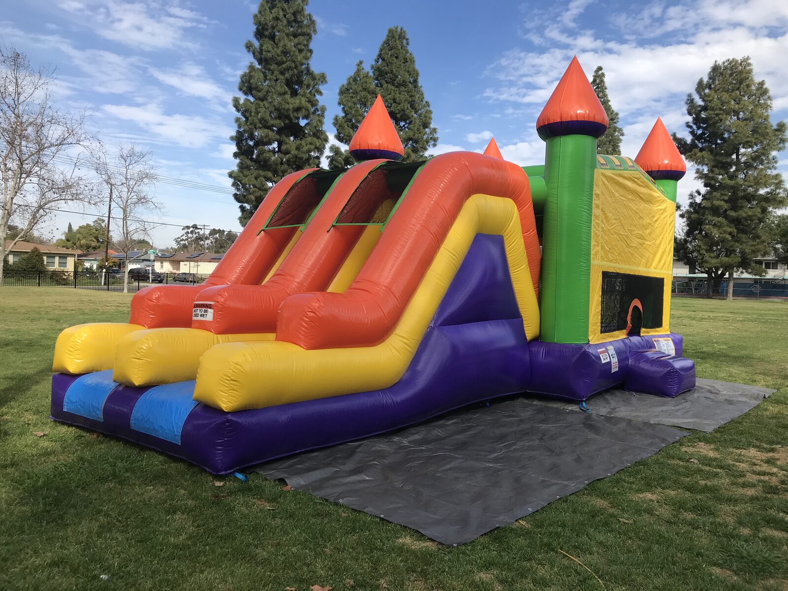 4n1 multi-color castle banner combo bounce house rental in San Diego, angled view of both covered slide lanes with the climb-up and orange safety walls