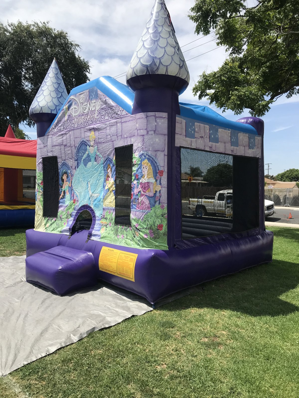 13x13 Disney Princess bounce house rental in San Diego — side-angled setup over a protective tarp showing the castle turrets and blue trim