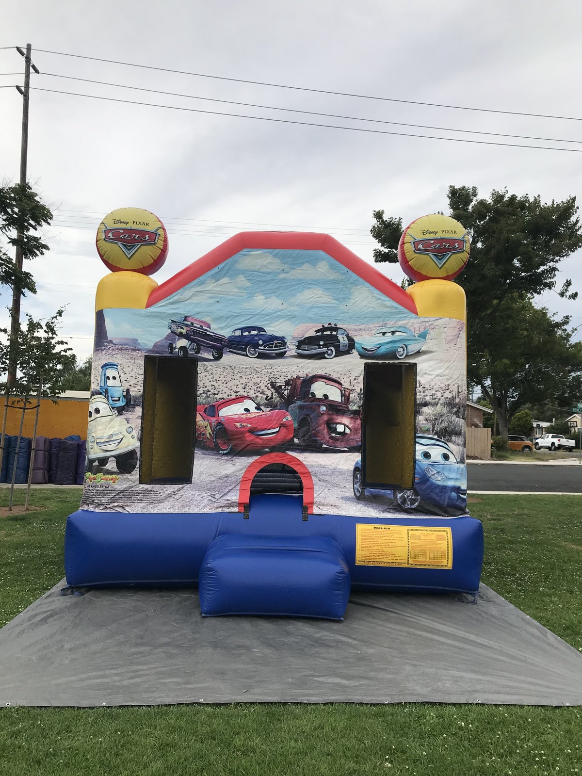 13x13 Disney's Cars bounce house rental in San Diego — straight-on front view over a protective tarp showing the red entry arch and safety rules panel
