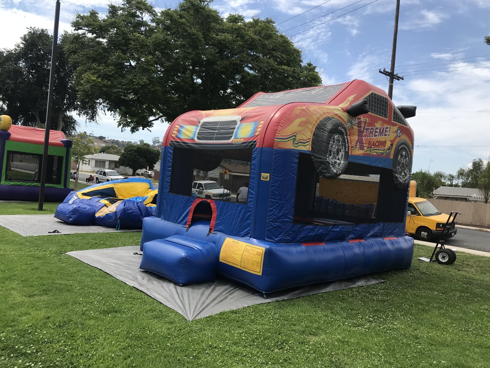 13x17 Xtreme Racer bounce house rental in San Diego — angled park setup on a tarp showing the Xtreme Racing side artwork and oversized tires