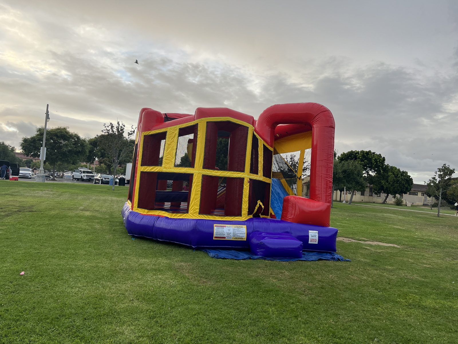 5n1 plain banner combo bounce house rental in San Diego, wide view of the red, yellow and purple unit with the curved slide arch on a park lawn