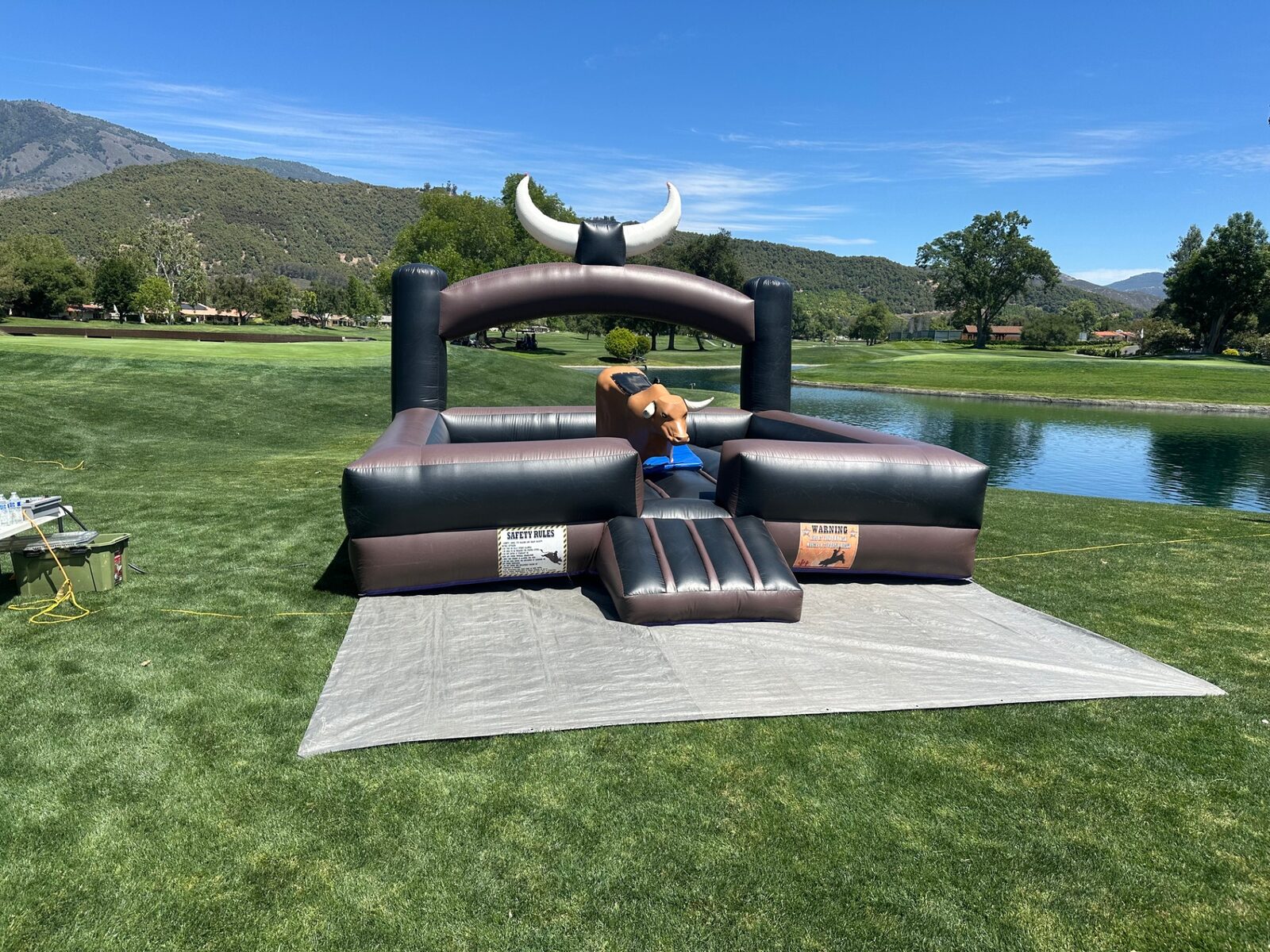 Mechanical bull rental in San Diego, 15x15 setup on a golf course lawn beside a pond with mountain views