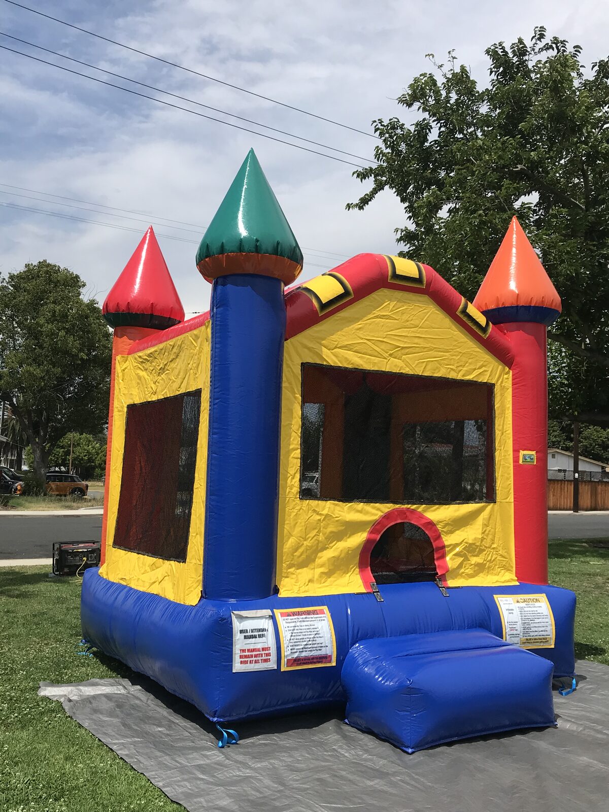 12x14 multi color castle mini bounce house rental in San Diego, three-quarter view showing the side mesh window and red turret