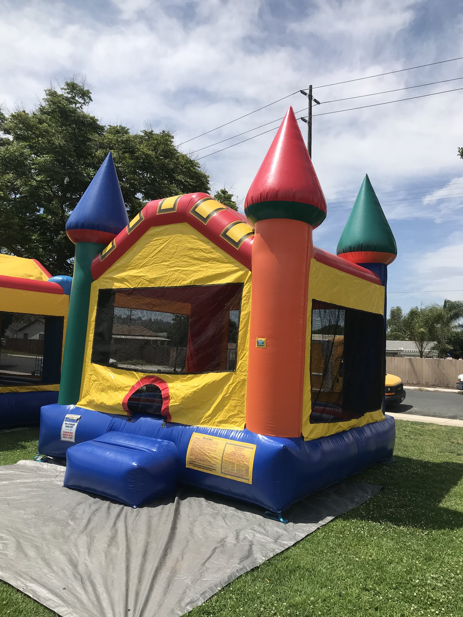 13x13 Multi-Color Castle bounce house rental in San Diego — side-angled view with the orange column, entry ramp, and rules panel visible