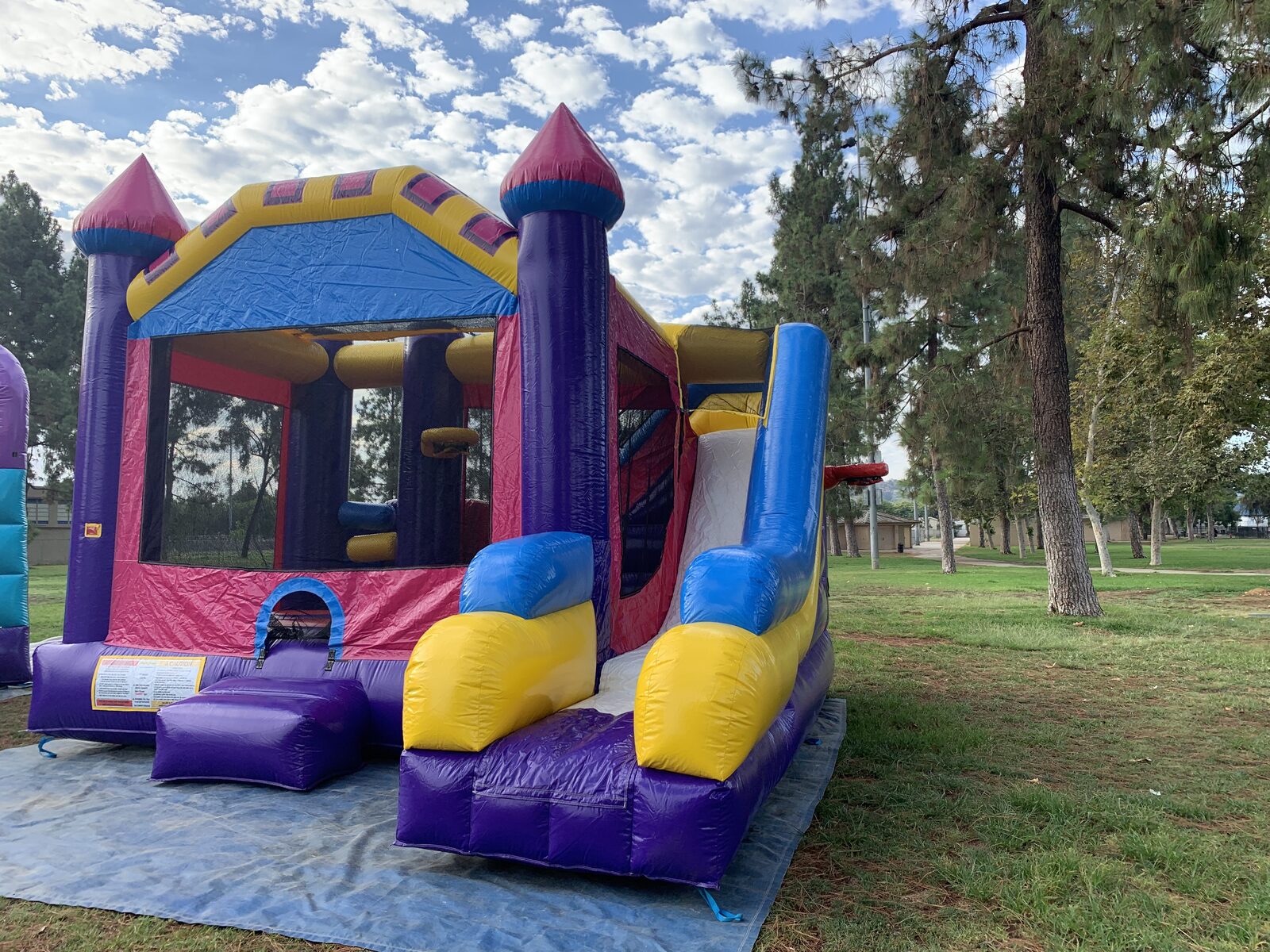 6n1 dream castle combo bounce house rental in San Diego, three-quarter view showing the interior obstacle columns and basketball hoop through the mesh window