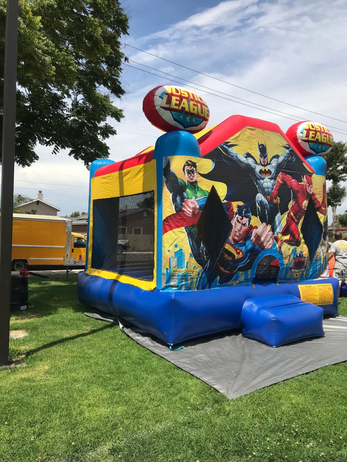13x13 Justice League bounce house rental in San Diego — angled view on a park lawn showing the mesh side windows