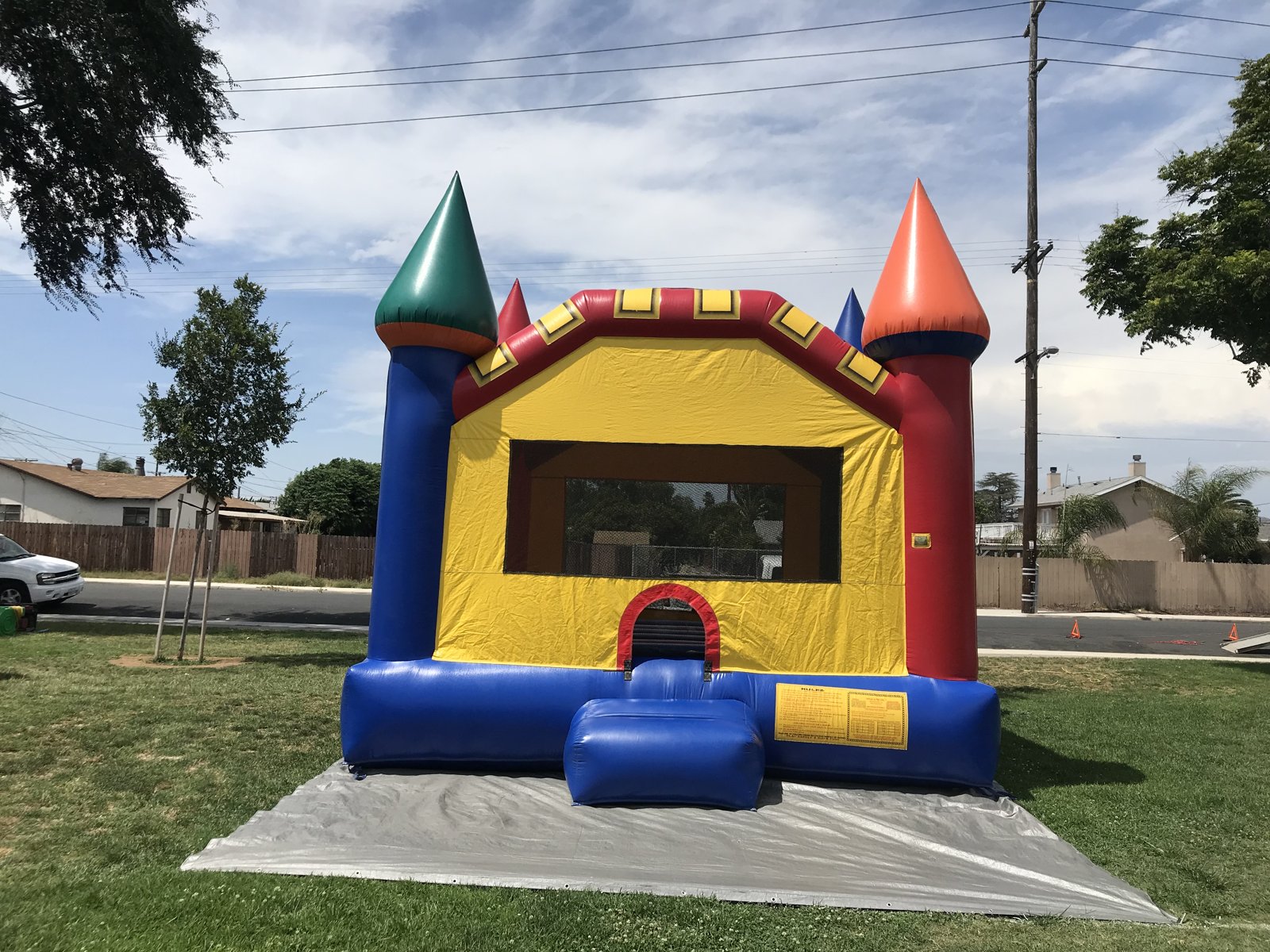 15x15 Multi-Color Castle bounce house rental in San Diego — straight-on front view with green, red, and blue turret toppers over a yellow front wall on a park lawn