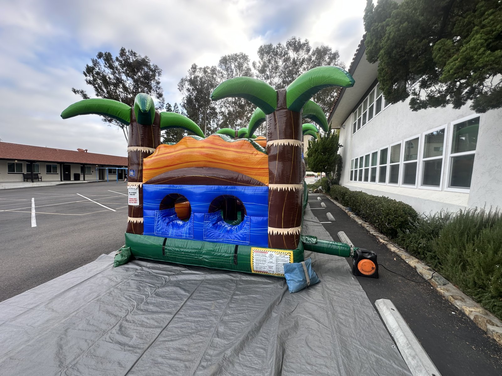 30ft tropical obstacle course rental in San Diego, front view of the twin crawl-tunnel entry with inflatable palm trees on a tarp