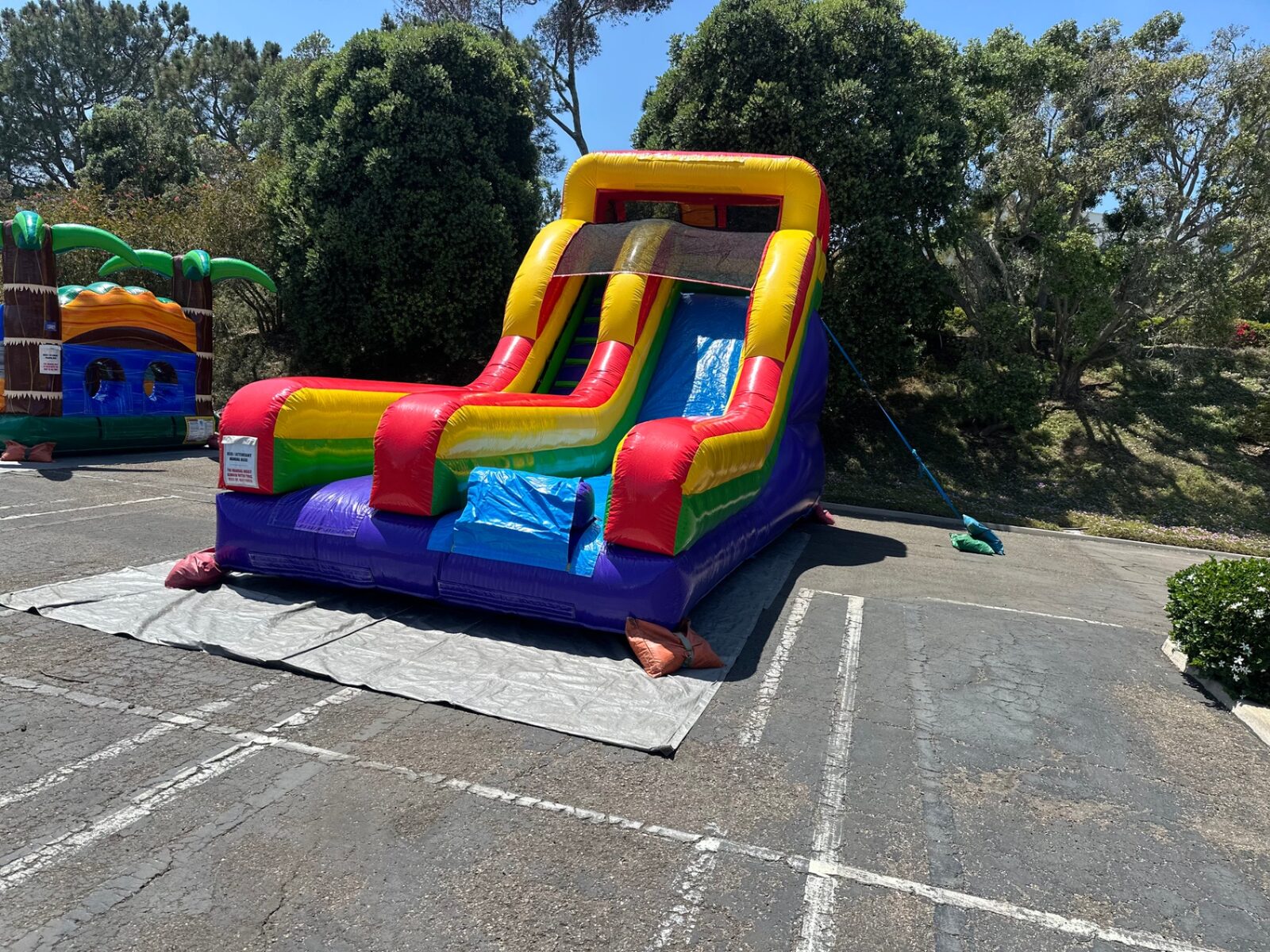Dry slide rental in San Diego, 15ft rainbow mini dry slide angled view beside a tropical bounce house
