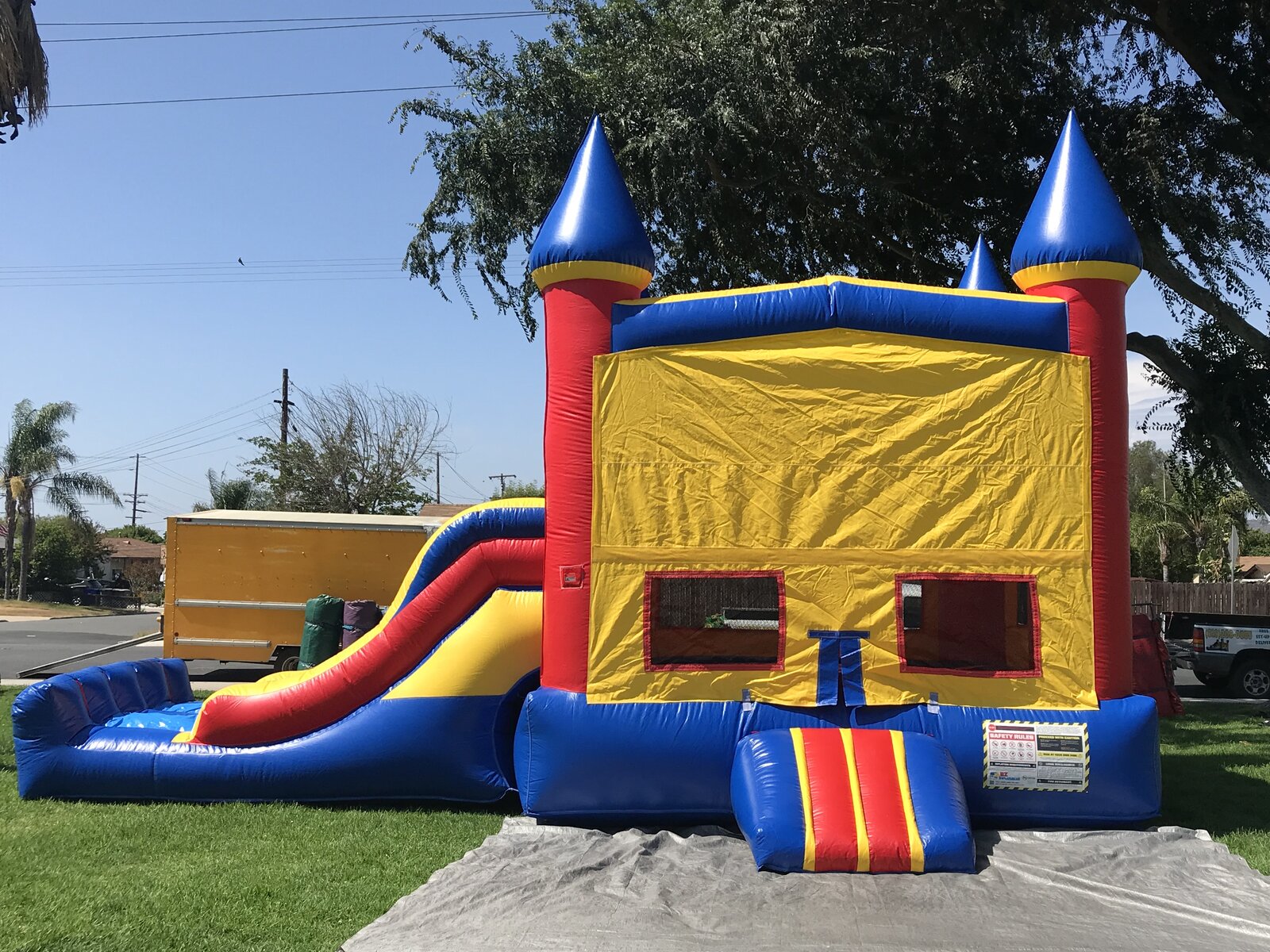 3n1 blue castle banner combo bounce house rental in San Diego, front view of the blue, red, and yellow castle with side slide staked on a tarp on grass