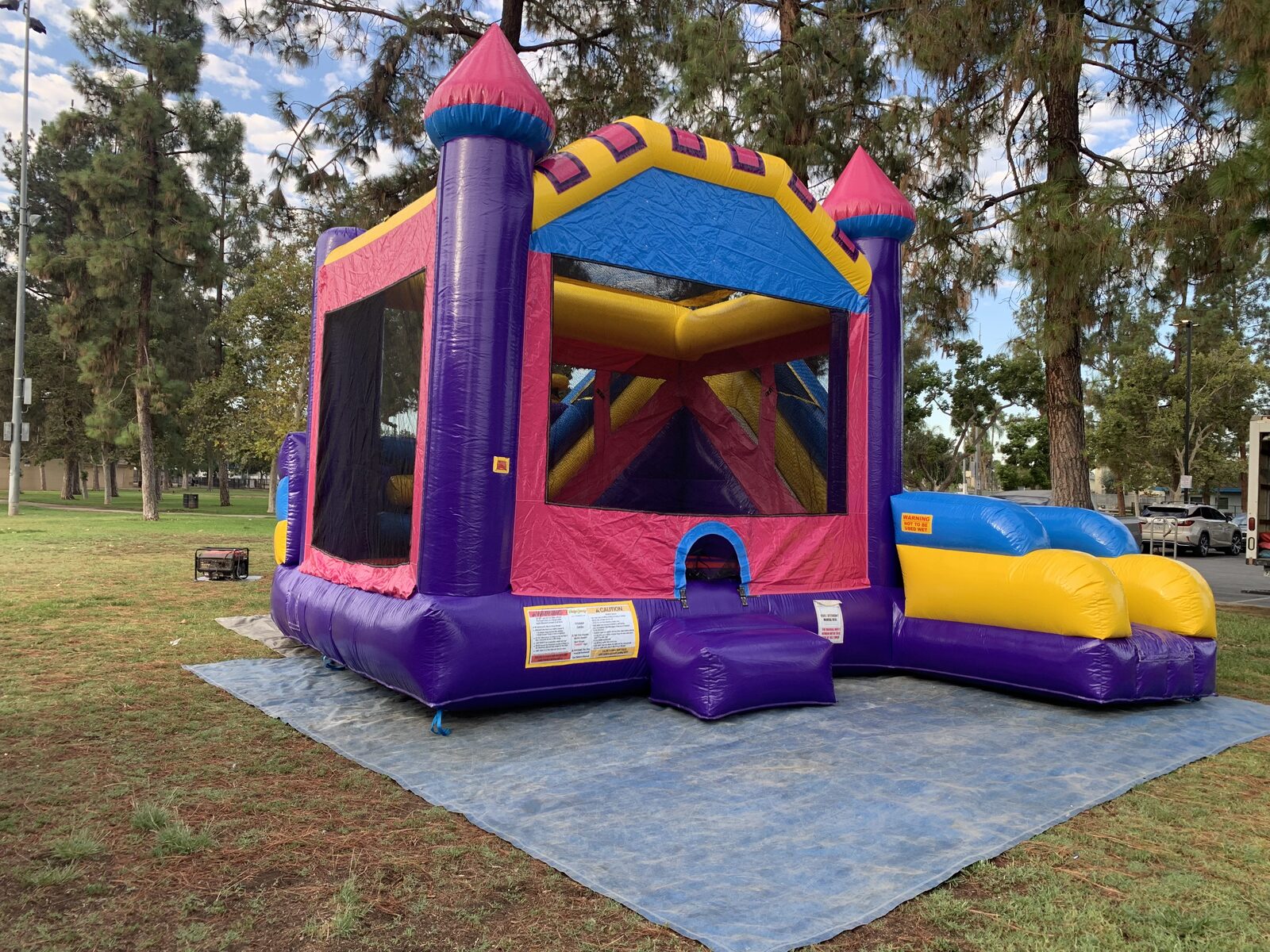 6n1 dream castle combo bounce house rental in San Diego, front view showing the entry step, mesh safety windows and generator setup on grass