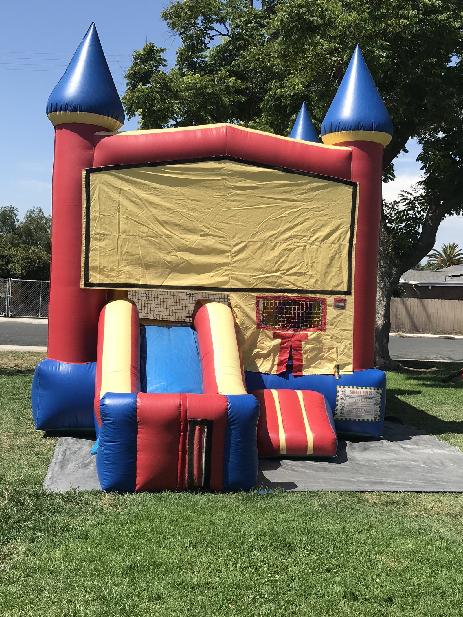 2n1 blue castle combo bounce house rental in San Diego, front view of the red, blue and yellow castle with side slide set up on grass