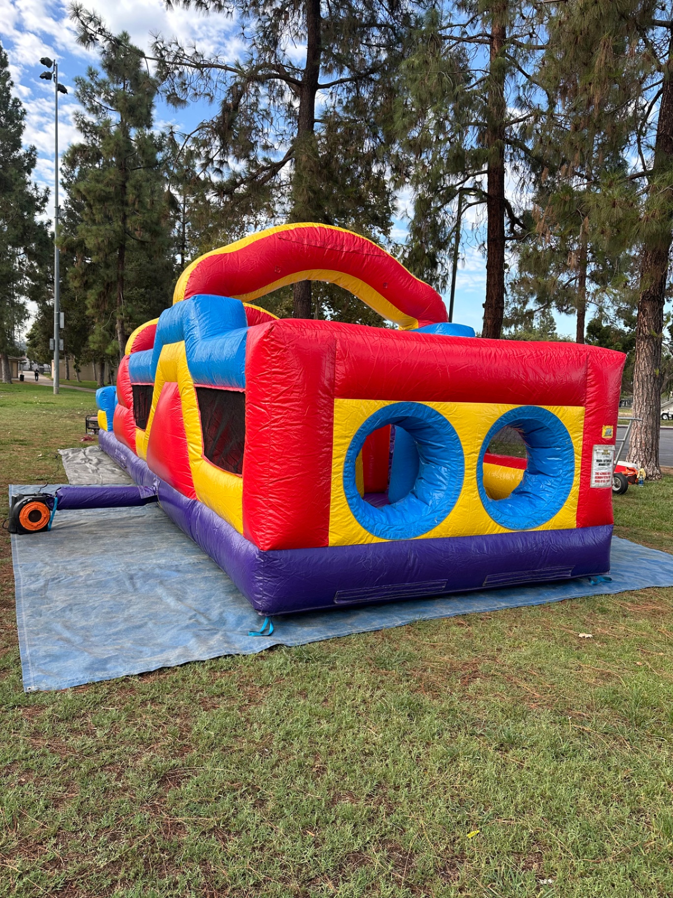 33ft monster obstacle course rental in San Diego, red, yellow, and blue course set up on grass at a park with crawl-through tunnels at the end