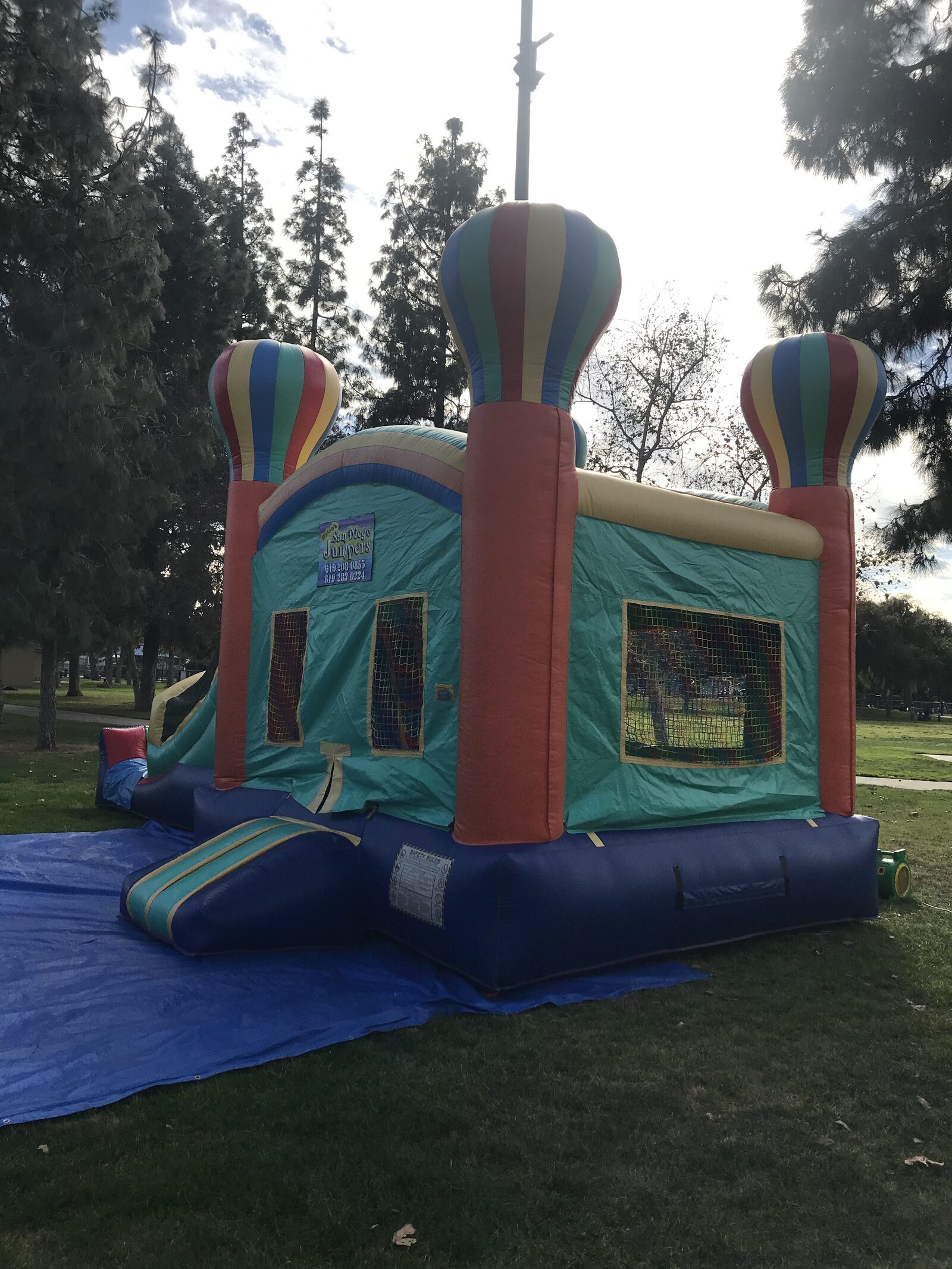 4n1 summer balloon combo bounce house rental in San Diego, front view of the teal and orange balloon castle with hot air balloon towers set up on a tarp at a park