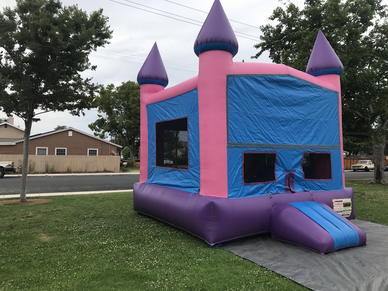 13x13 Pink Castle Banner bounce house rental in San Diego — angled side view on a grass lawn showing the entry ramp and mesh windows